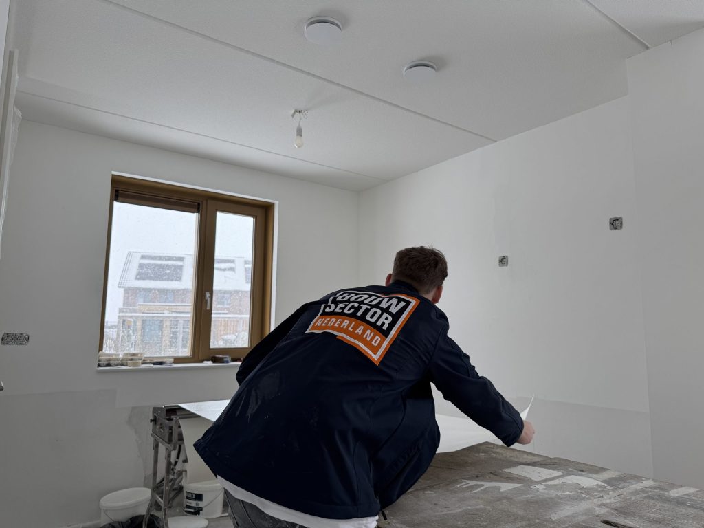 Vakman van Bouwsector Nederland in werkjas legt een baan behang op de plaktafel