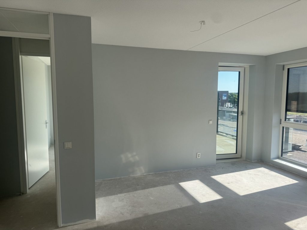 Kamer in een appartement met lichtgrijze wanden, een balkondeur en een groot raam