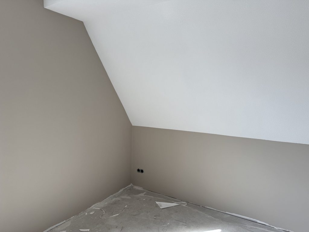 Zolderkamer met een schuine wand en strak afgewerkte muren in een warme grijstint